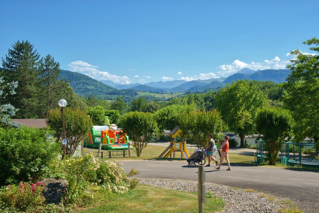 Famille en balade dans un camping 3 étoiles en Ariège, avec aire de jeux pour enfants et vue sur les montagnes des Pyrénées.