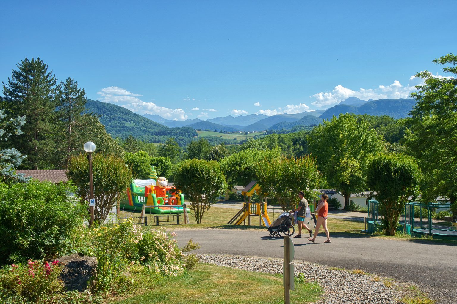 Famille en balade dans un camping 3 étoiles en Ariège, avec aire de jeux pour enfants et vue sur les montagnes des Pyrénées.