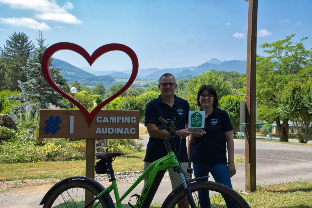 Bruno et Bénédicte, gérants du Camping Audinac-les-Bains, posent avec le label Accueil Vélo, un camping idéal pour le cyclotourisme et les vacances à vélo dans les Pyrénées.