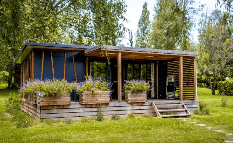 Chalet Premium climatisé avec grande terrasse en bois décorée de jardinières fleuries au Camping Audinac les Bains en Ariège