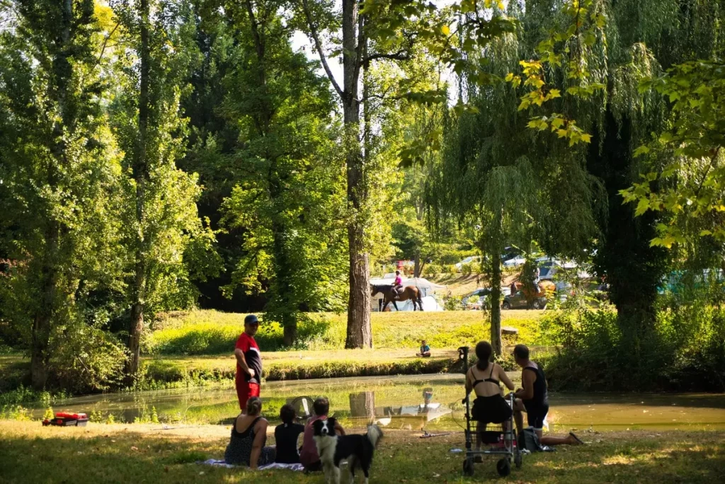 Familles se détendant au bord de l'étang dans le parc arboré du Camping Parc d'Audinac les Bains, camping famille en Ariège
