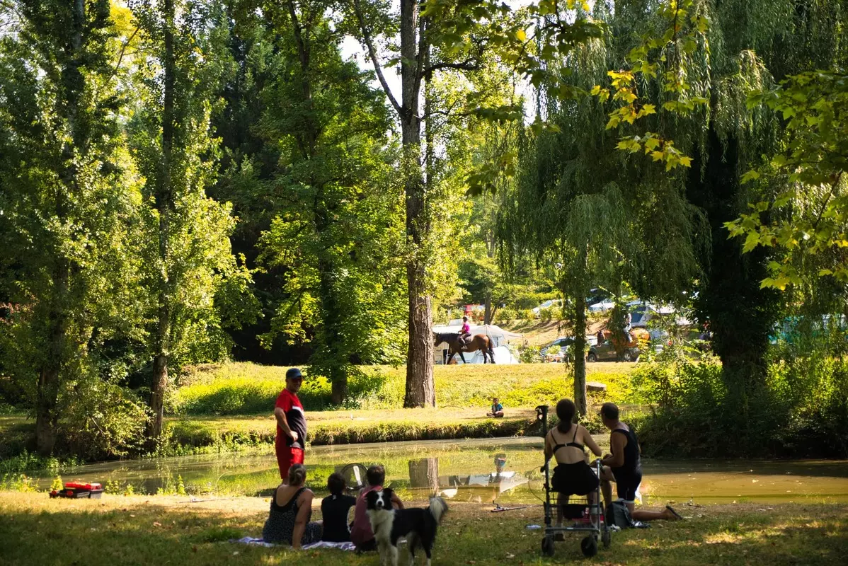 Familles se détendant au bord de l'étang dans le parc arboré du Camping Parc d'Audinac les Bains, camping famille en Ariège