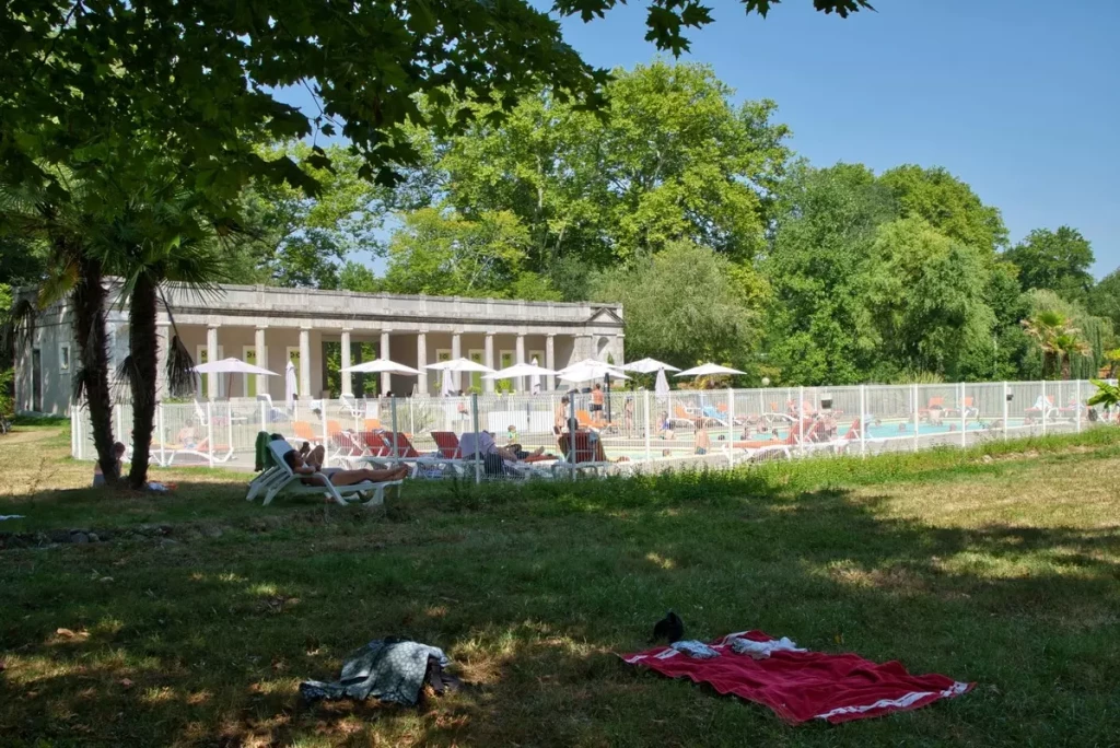 Piscine chauffée avec transats et parasols au Camping Parc d'Audinac les Bains, entourée d'arbres en Ariège